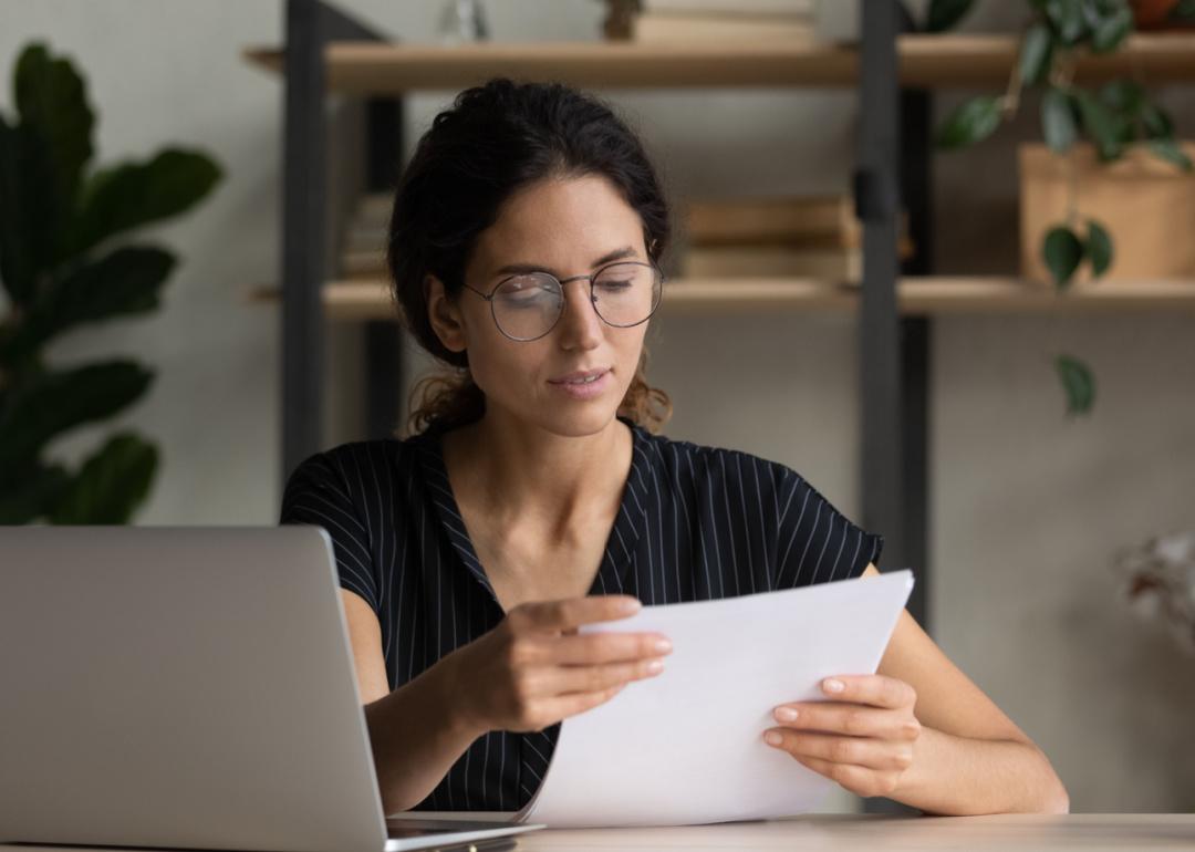 Person sitting at desk with open laptop looking at documents.