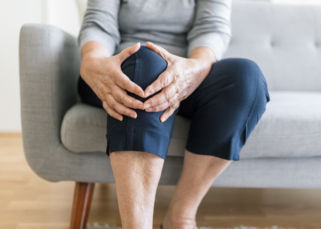 Cropped view of seated person holding knee.