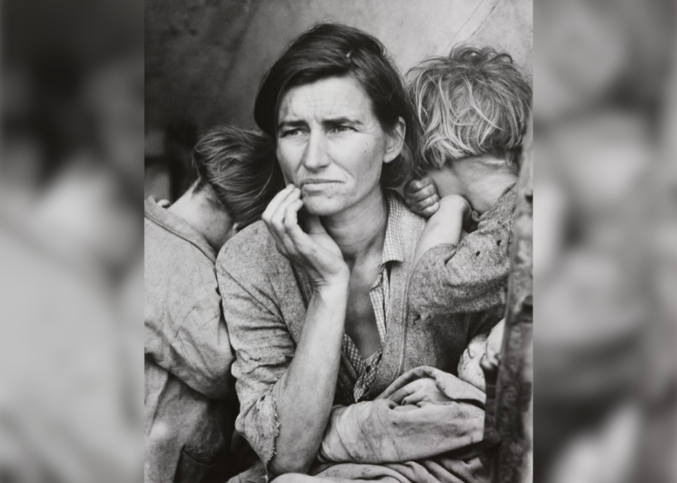 A woman with her hand to her face holding an infant with young two children facing away from the camera.