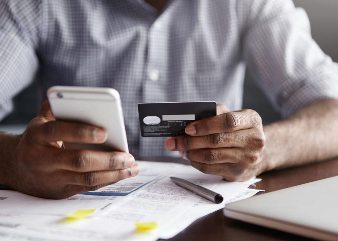 Person paying bills looking at credit card and phone.