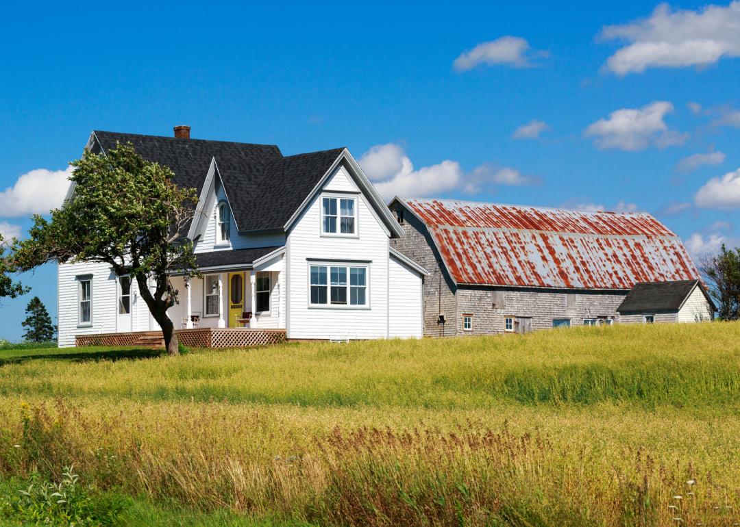 White farmhouse sits in a field with barn in rear.