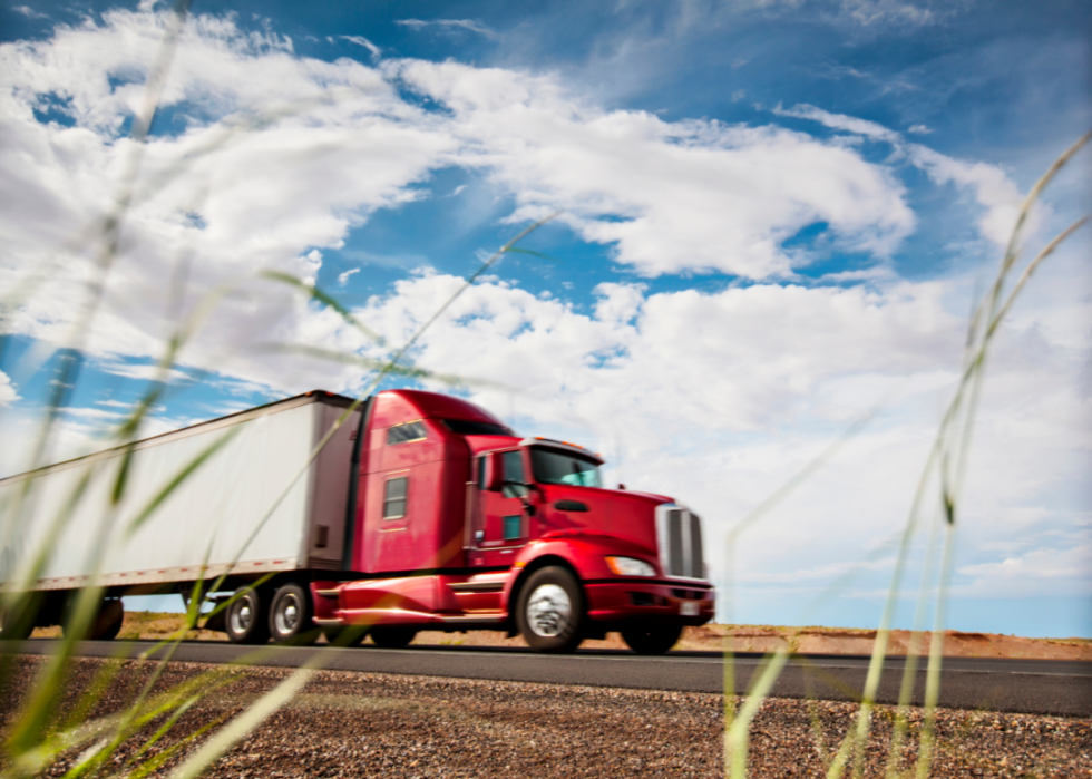 A red semi truck speeds along a highway