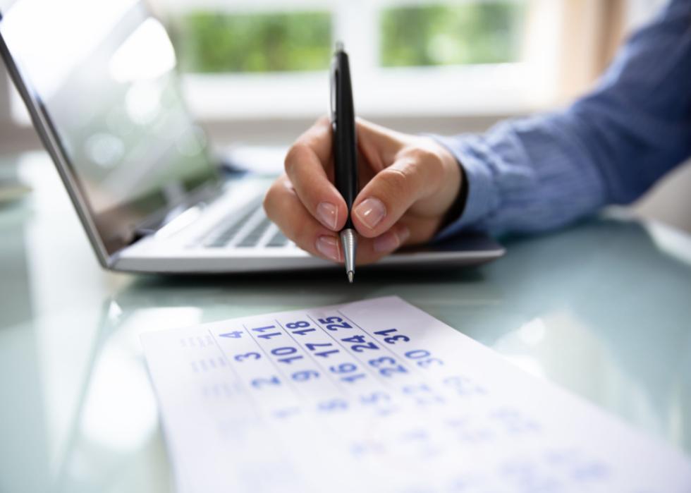 Close up on hand and calendar beside laptop