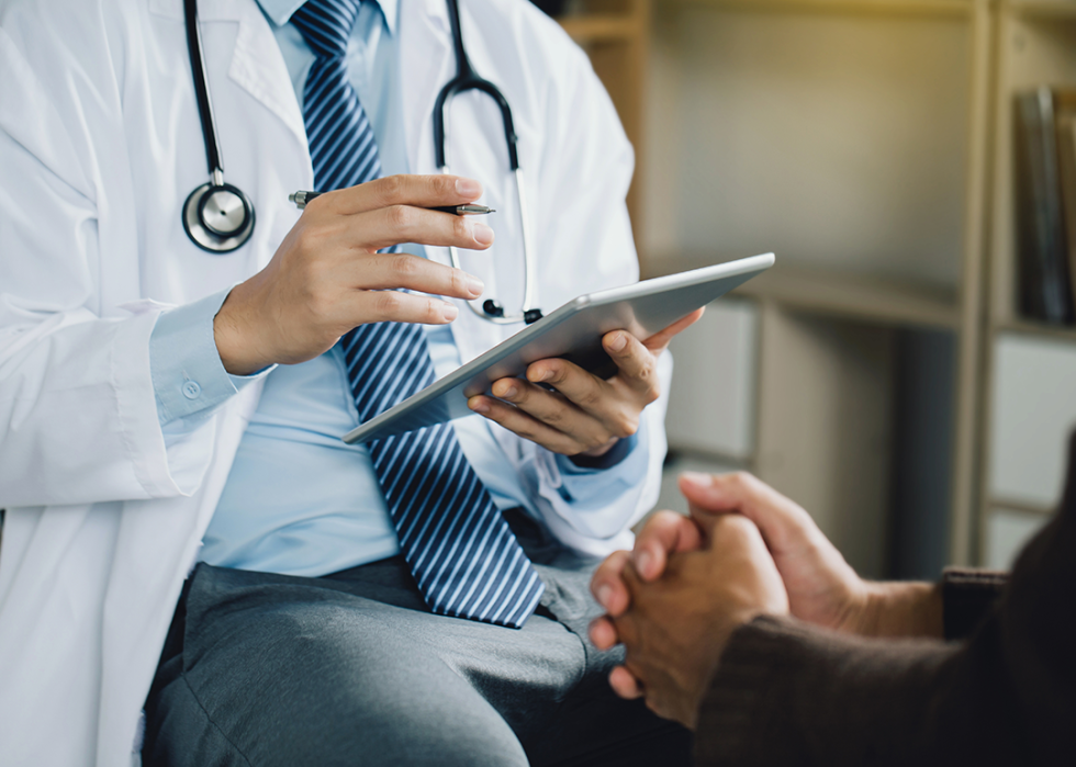 Doctor holding a tablet, speaking with patient.