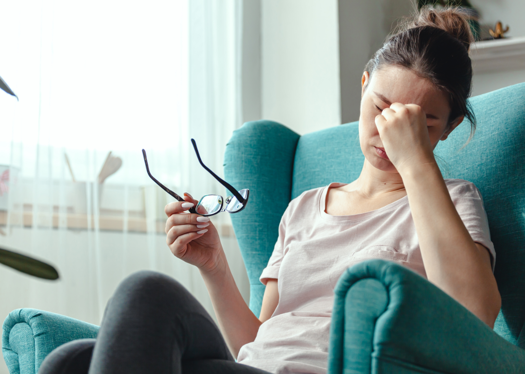 Woman sitting in chair holding head.