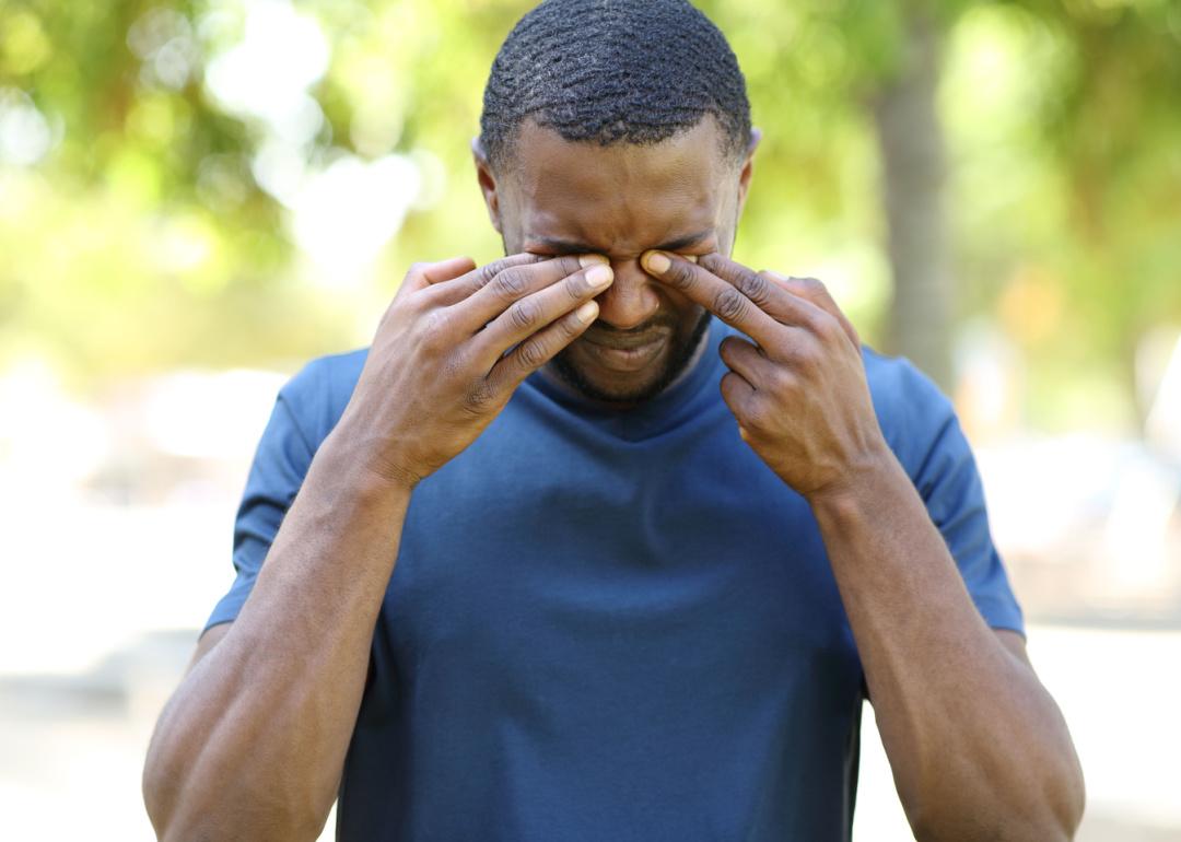 Man rubbing eyes outside.