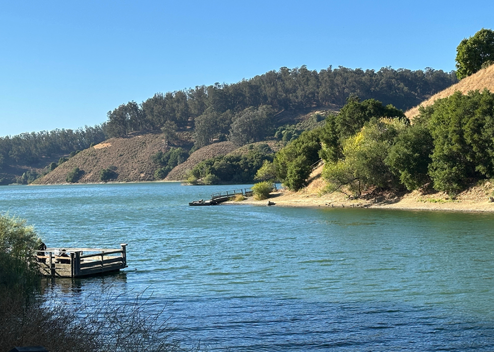 Wooden dock on the shore of a peaceful lake, with surrounding forested hills.