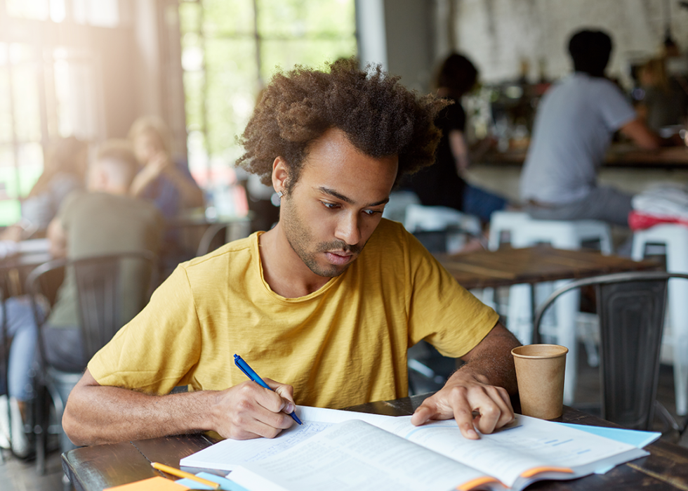 College-aged person studying at coffee shop, writing in a notebook..
