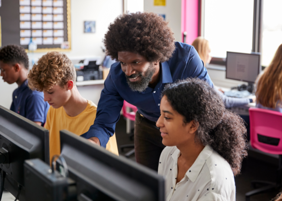 A teacher instructs a female student looking at a computer monitor