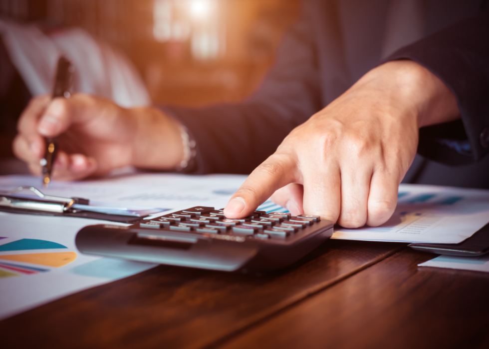 A man's hand calculates figures while reviewing documents