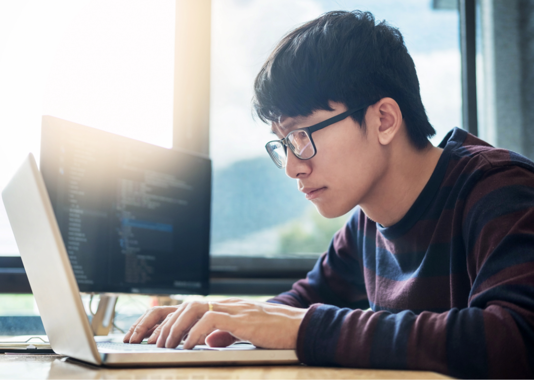 A young man with glasses looks skeptically at his laptop.