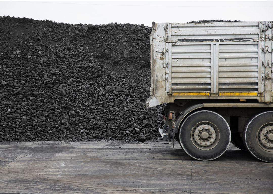 The rear trailer of a truck sits in front of a big pile of coal at a mining site.