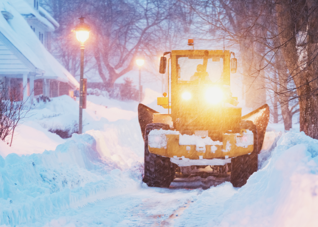 A snowplow passes through a village at sunset.