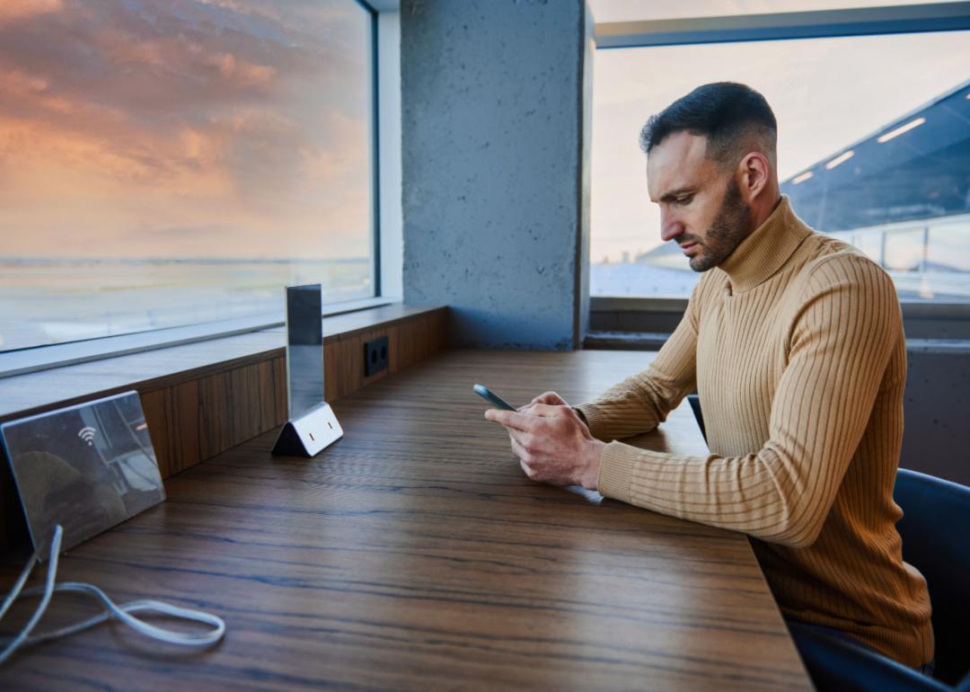 A person on multitasks on their phone and laptop in an airport coworking space.