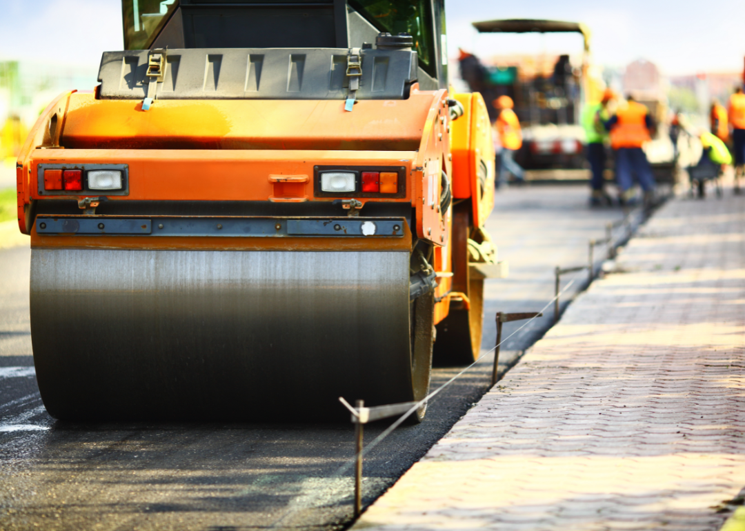 Road construction with a steamroller in the foreground and workers in the background.