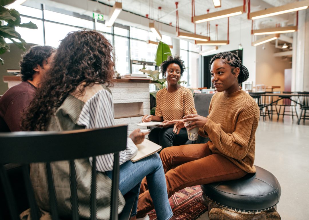 A group of people sit in a circle in an open office talking.