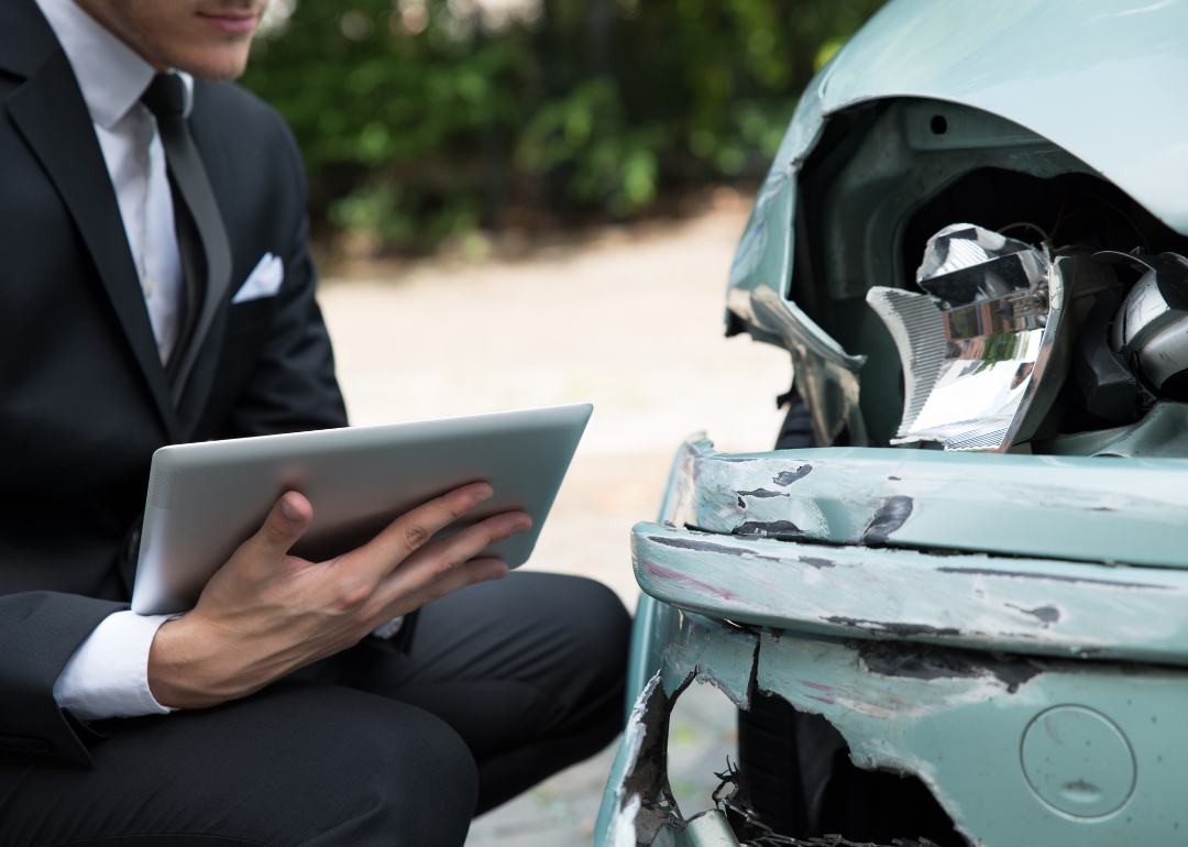 Insurance agent takes notes as he looks at damaged car.
