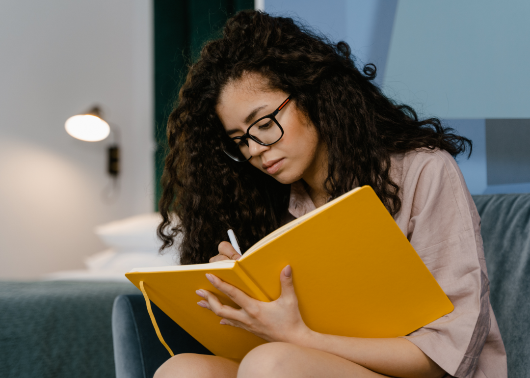 A woman writes in a journal with a yellow cover.