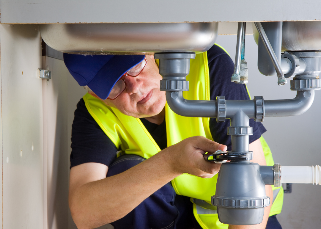 A plumber tightens a pipe under a sink.
