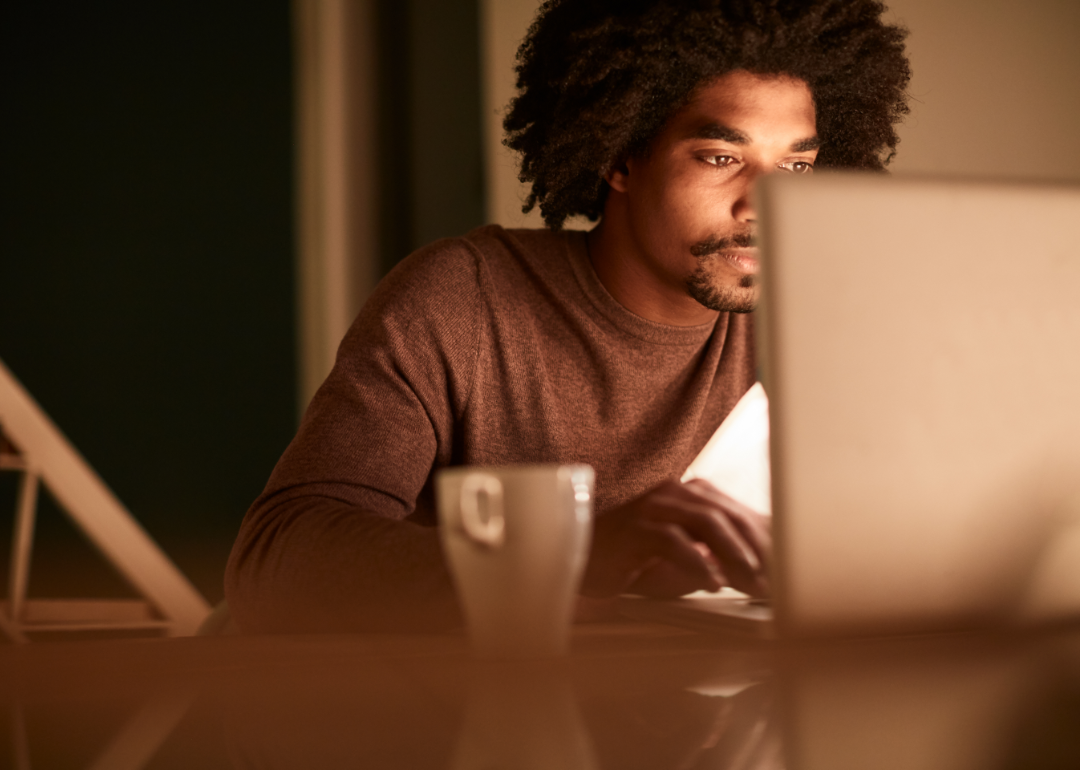 A man studies information on his laptop with a coffee cup in the foreground.