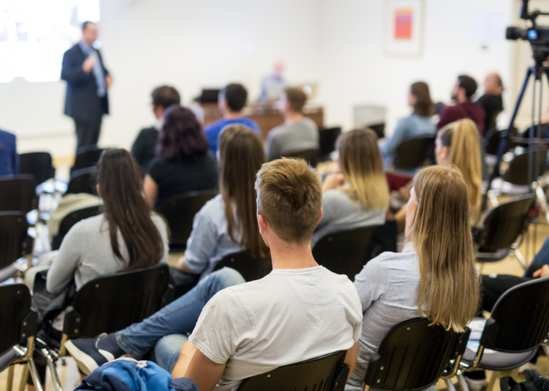 Students listen as a professor speaks in a college lecture hall.