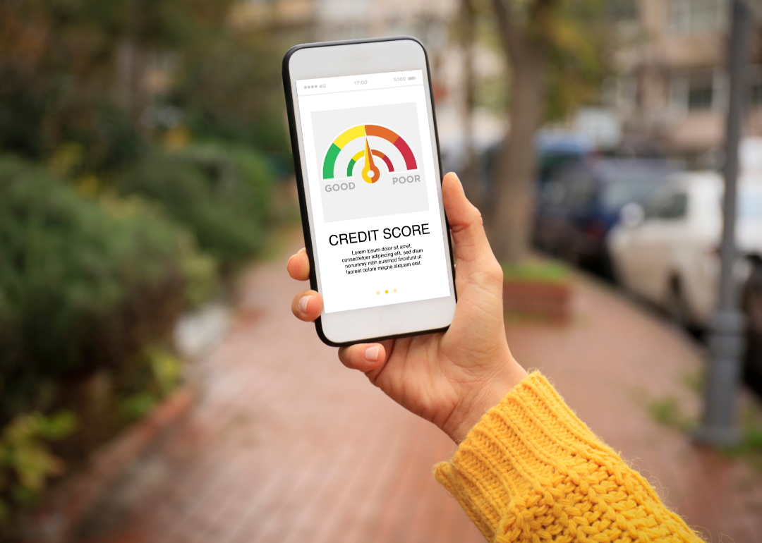 A person wearing a yellow sweater examines their credit score on their phone.
