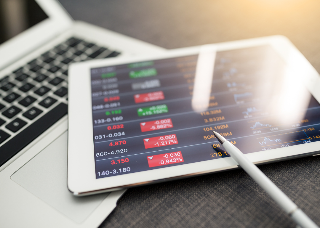 Tablet displaying investing information sitting on top of laptop.
