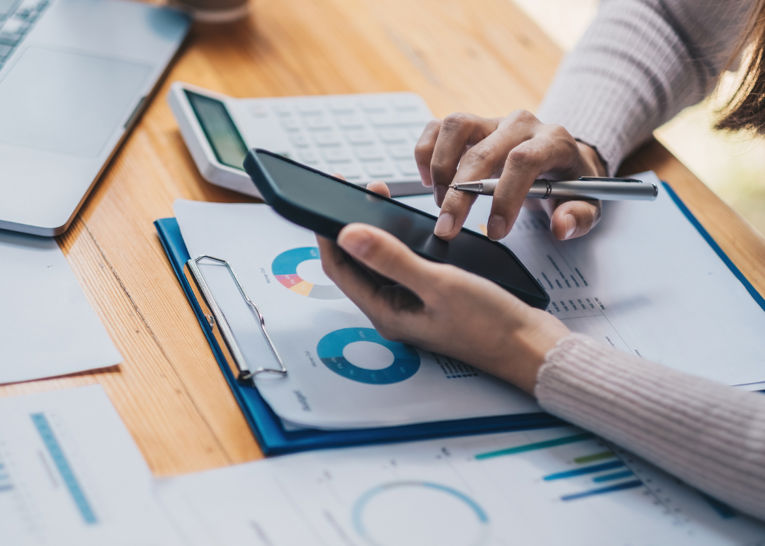 A woman uses a calculator at a desk covered with financial charts.
