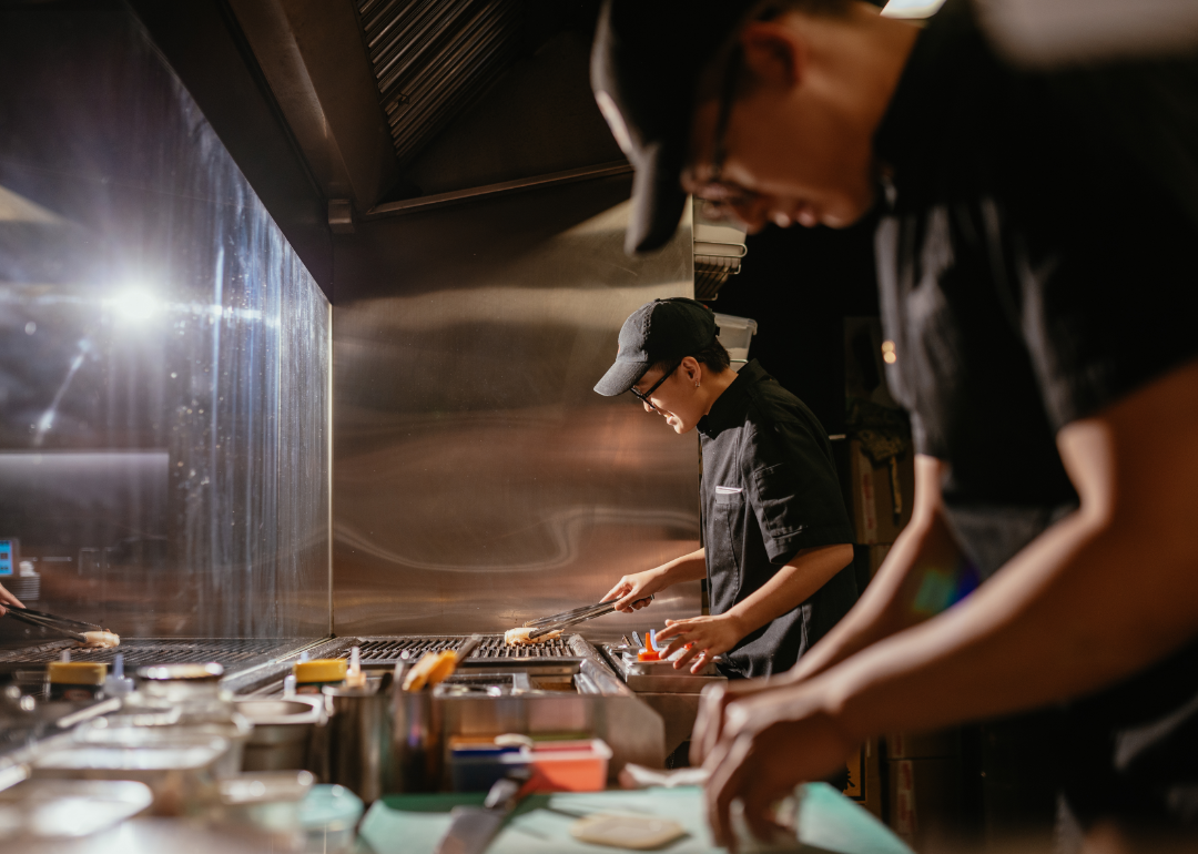 Chefs in a professional kitchen work on plating food.