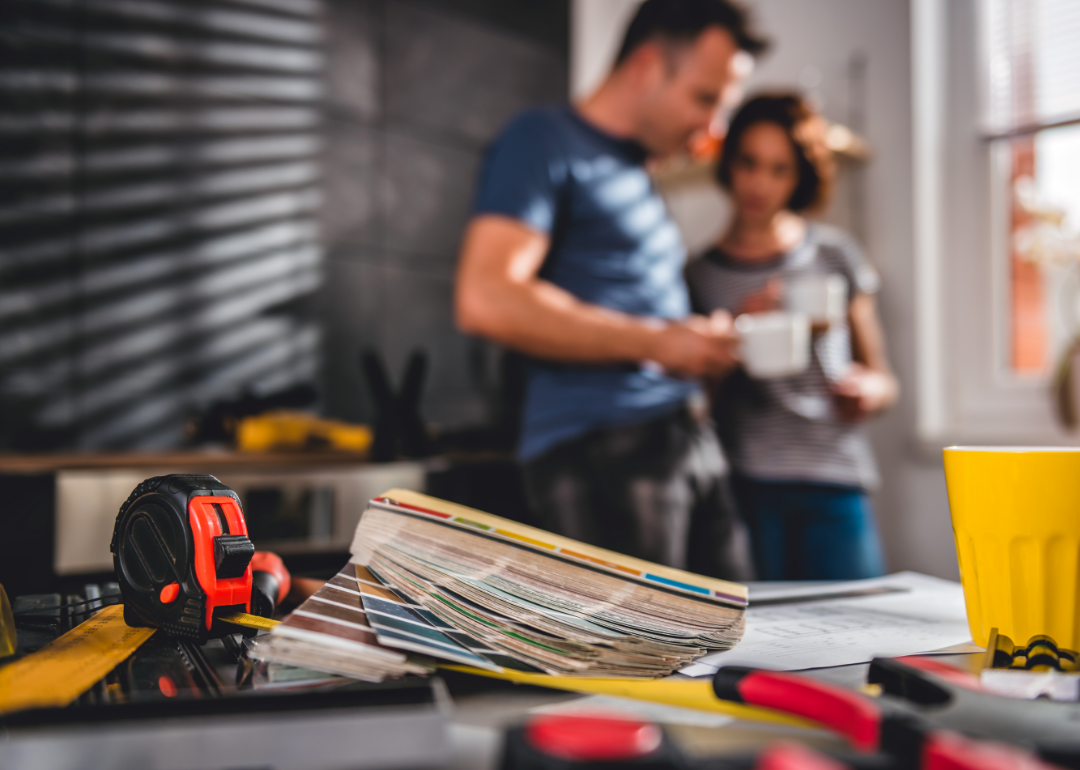 Couple talks behind a table covered with repair tools and measuring tape.