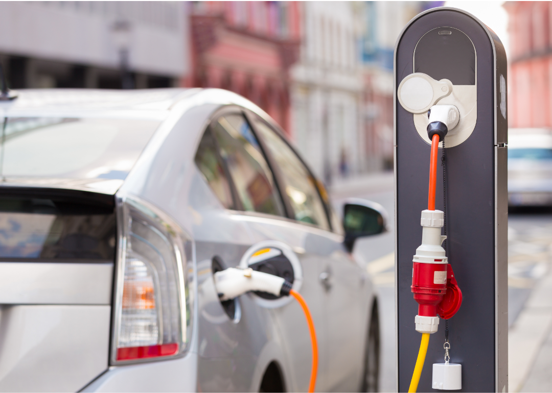 A white electric Toyota Prius sits parked on a street as it charges at a charging station.
