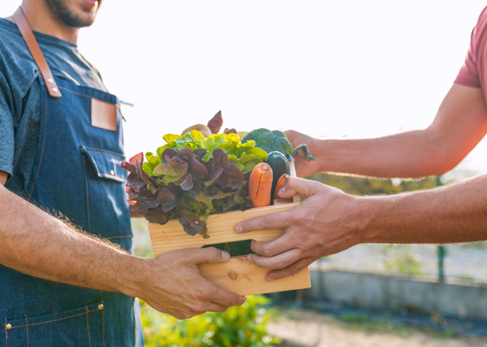 Farmer hands a box of vegetables over to a customer