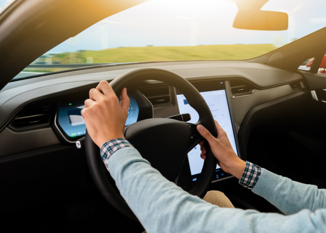 Person behind the wheel of an electric car driving down the road in the sunlight.