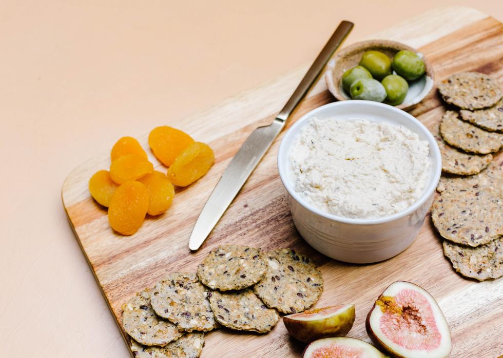 A vegan artisanal cheese on a cutting board with crackers, fruits and vegetables.