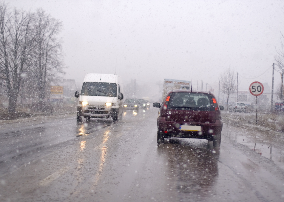 Windshield view of car driving through snowy and rainy weather.
