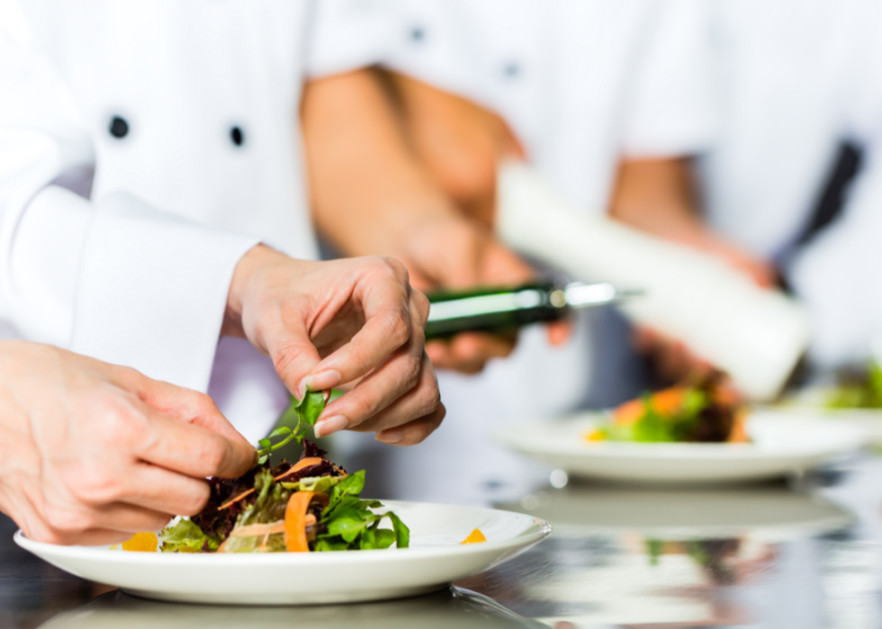 Two chefs preparing salads in a restaurant kitchen.