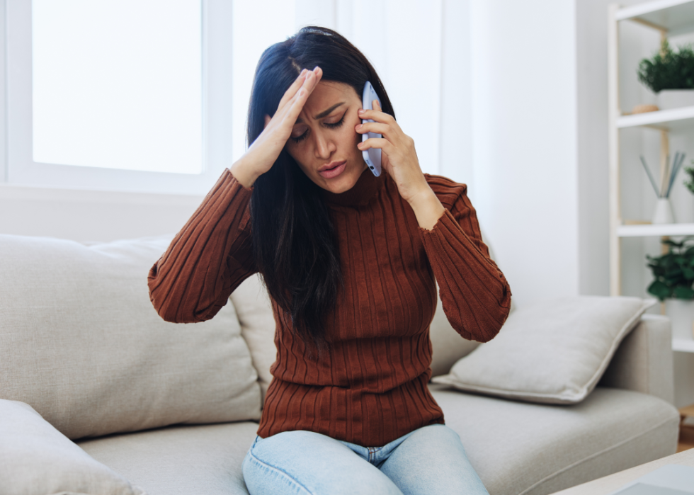 Frustrated woman sits on couch talking on the phone.