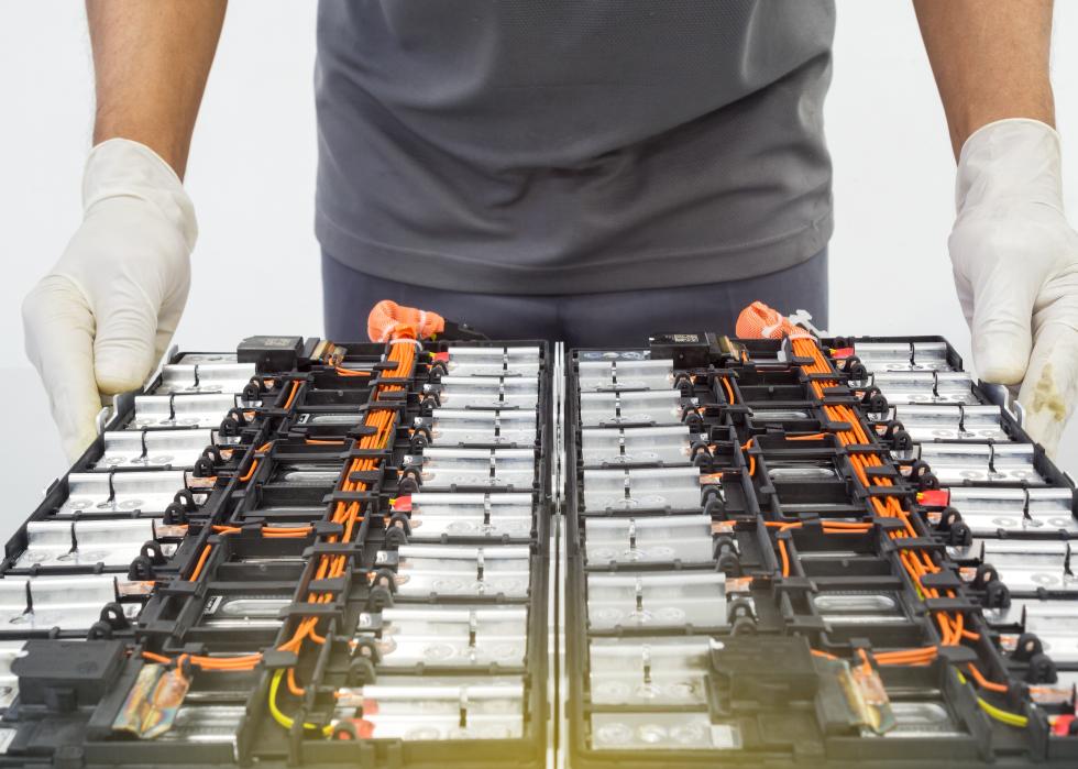 Selective focus on the rubber-gloved hands of an expert technician holding a used Lithium-ion car battery before its repair