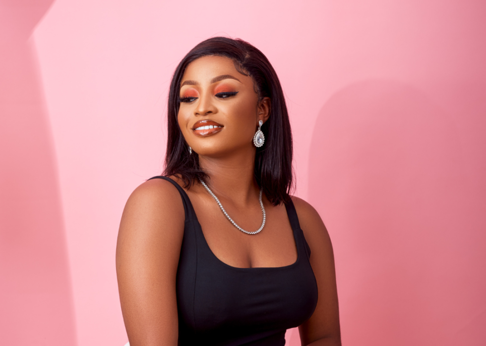 Black woman striking pose in black dress in front of pink background.