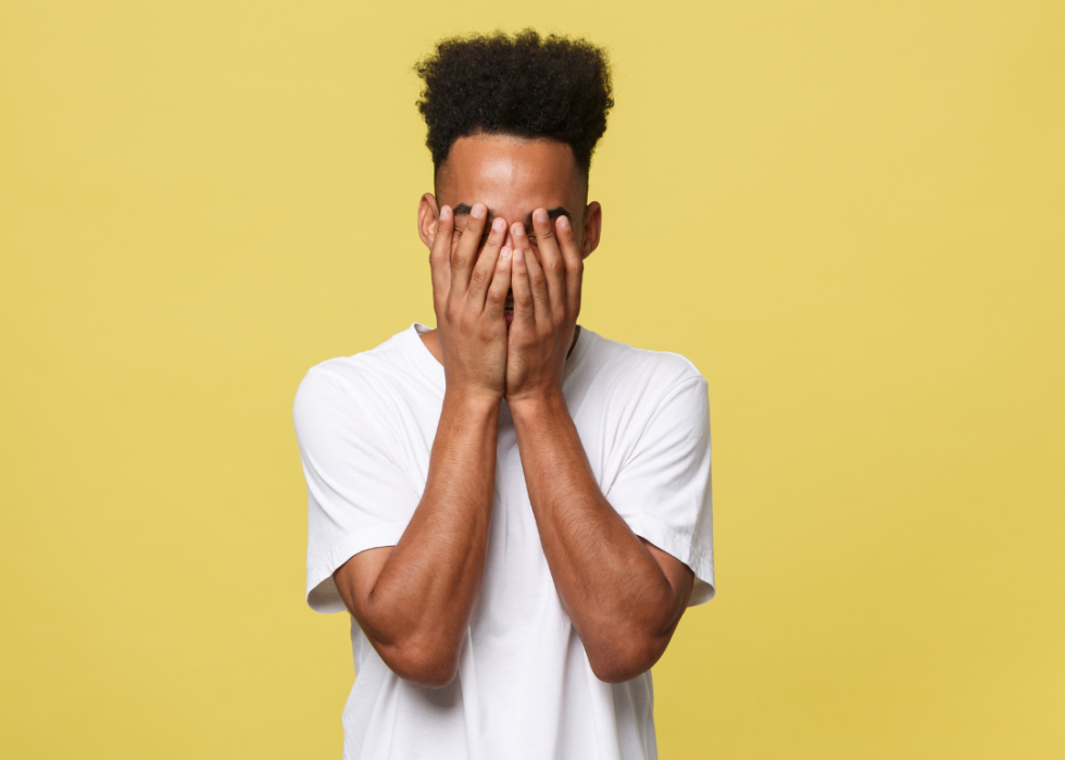 Black man wearing white T-shirt with hands pressed against his face in disappointment.