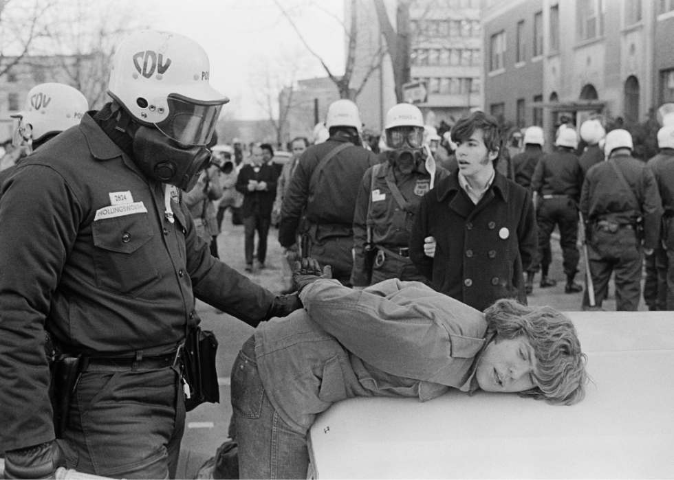 Police wearing helmets and gas masks arrest anti-war demonstrators.