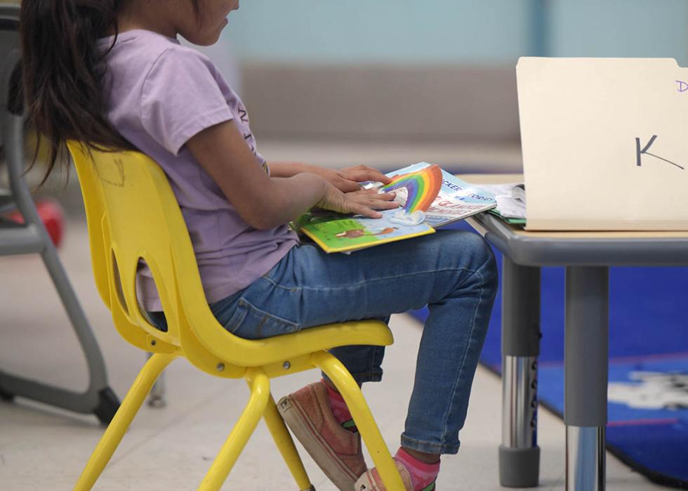 A young girl enrolled in Havasupai Elementary school is sitting inside a classroom reading a children's book.