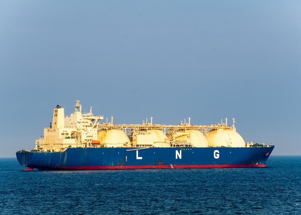 A blue colored hull large liquefied natural gas (LNG) carrier with 4 LNG tanks sails along the sea.