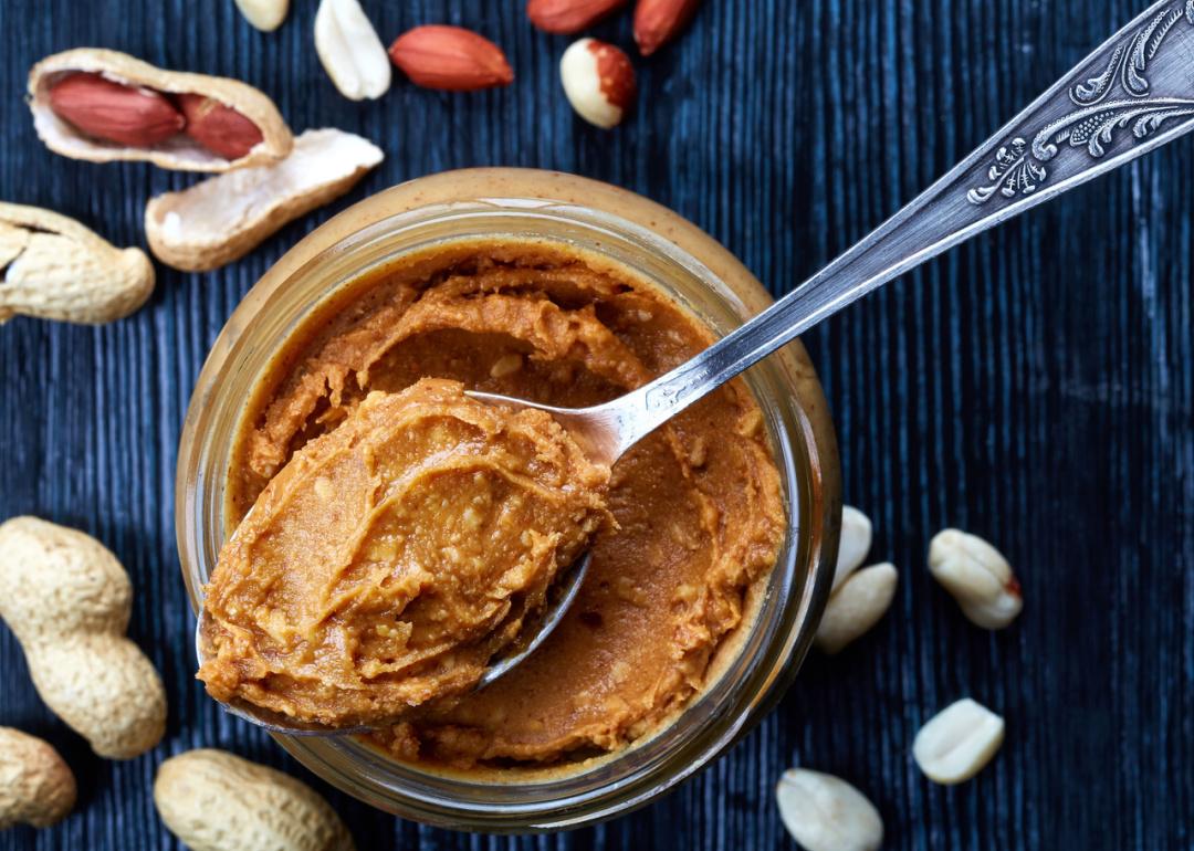 Jar and spoon of peanut butter and peanuts.