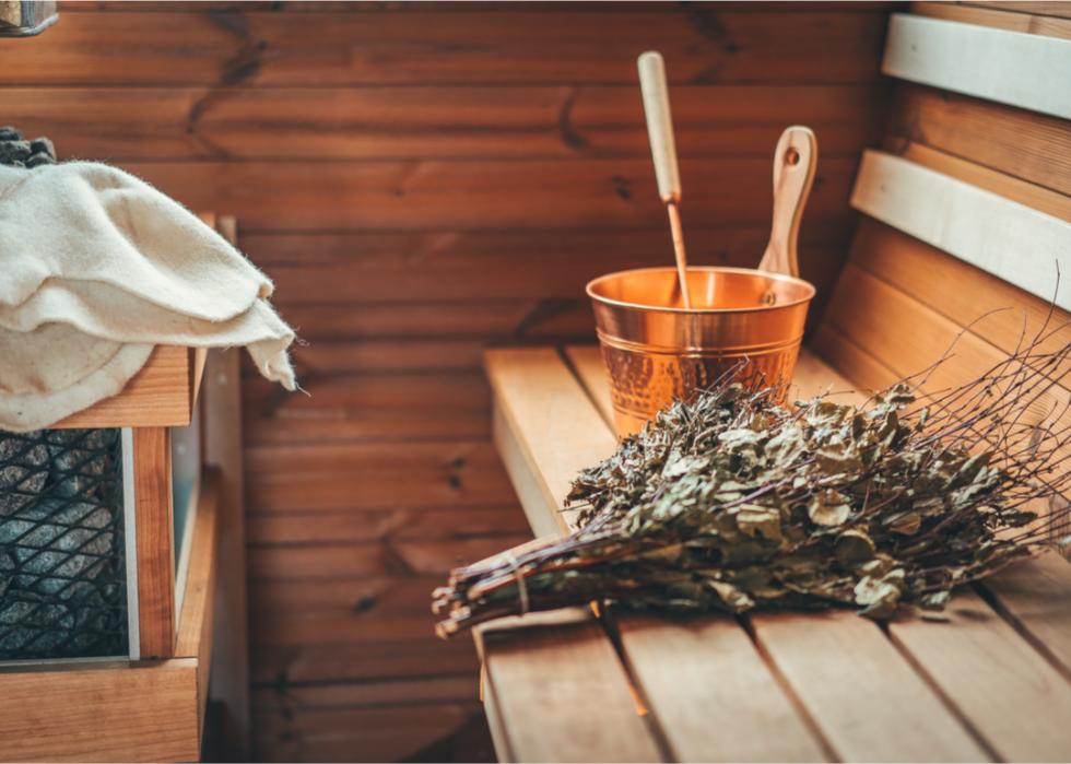 The inside of a sauna with a bunch of herbs and a copper bucket on the bench.