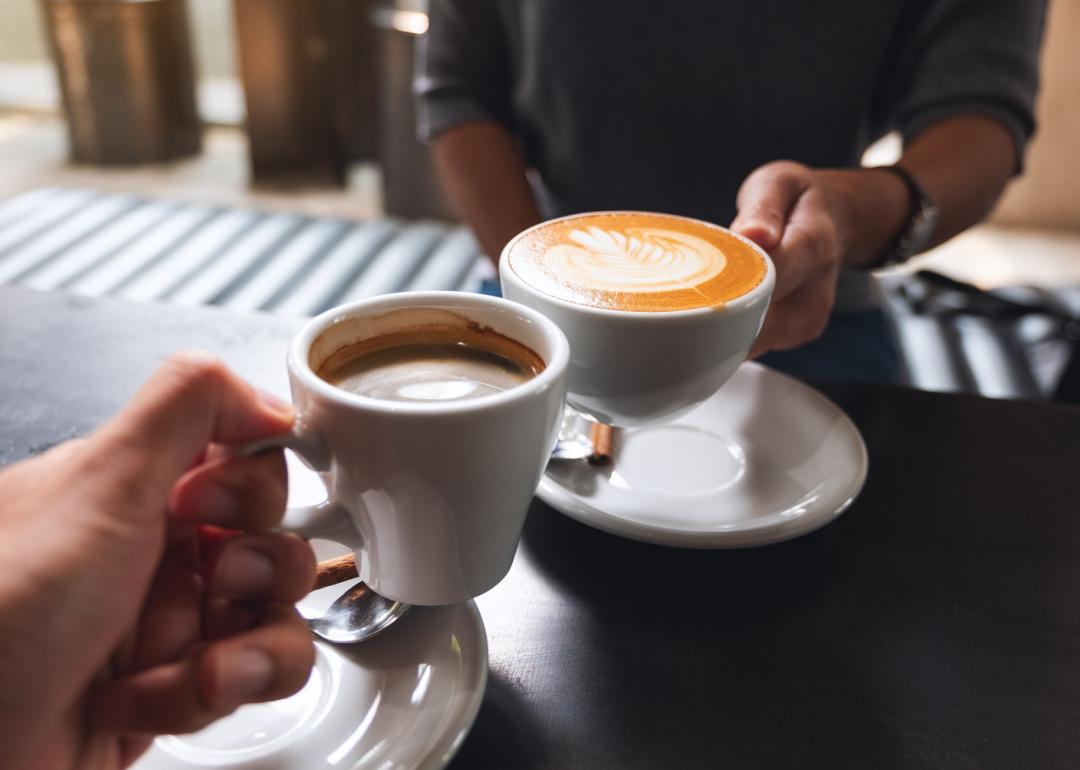 Two people clinking coffee mugs in cafe.