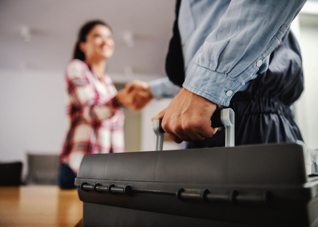 Person shaking hands with a repairman while standing at home.