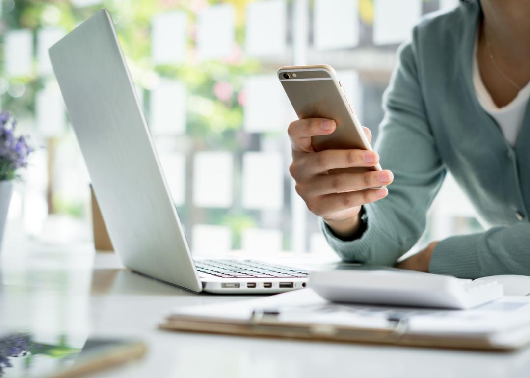 Person holding phone with open laptop.