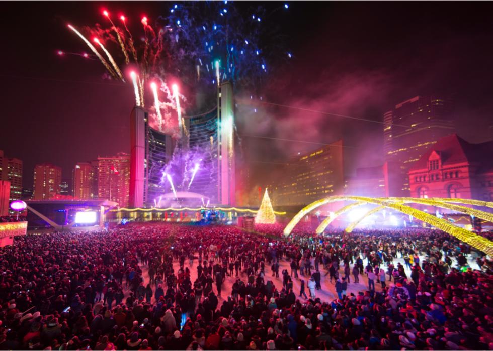 Massive crowds gather to watch a firework show coming from a tall building.