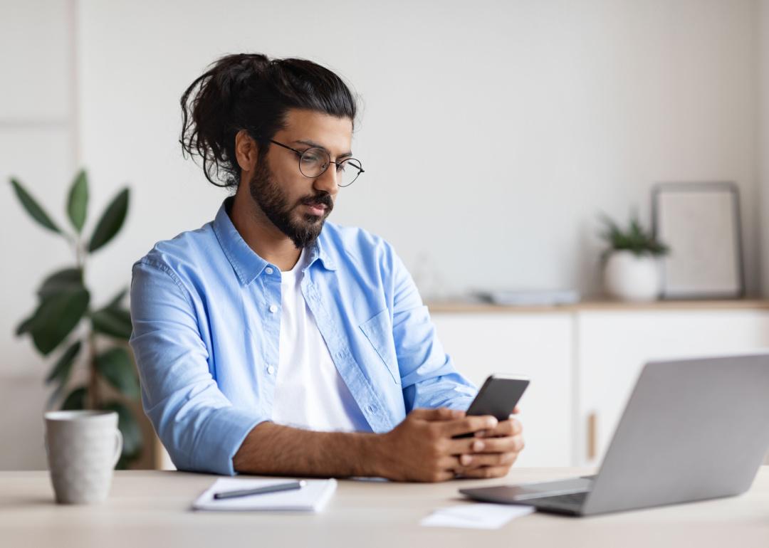 Person with glasses looking at phone and laptop.